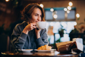 Junge Frau trinkt Kaffee im Café und isst ein Croissant