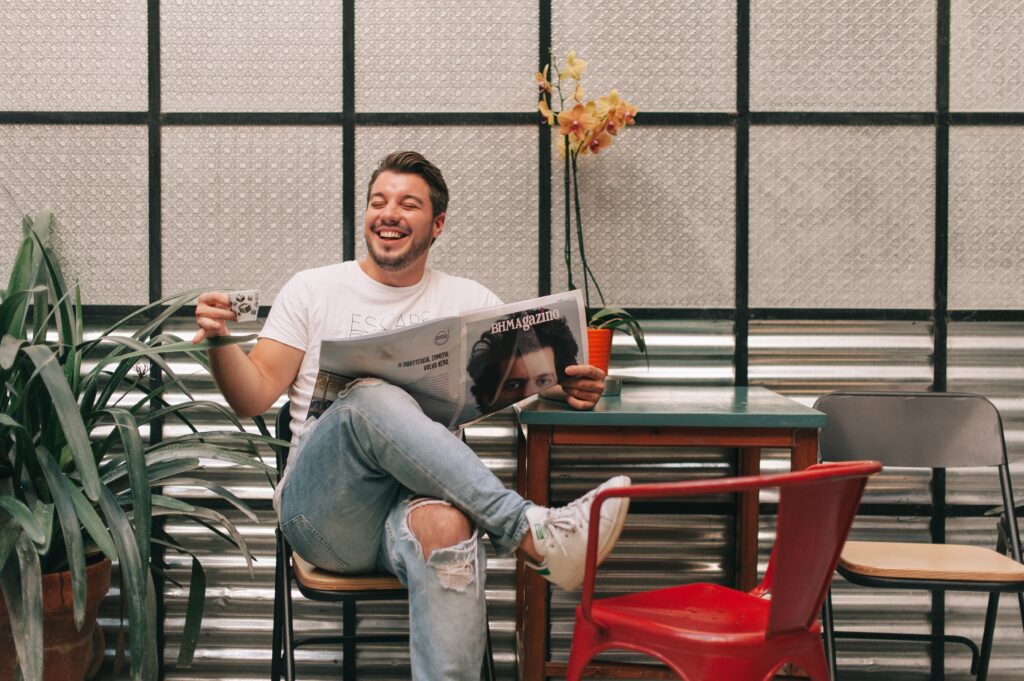 Fröhlicher Mann im Café, mit Zeitung, neben ihm roter Stuhl